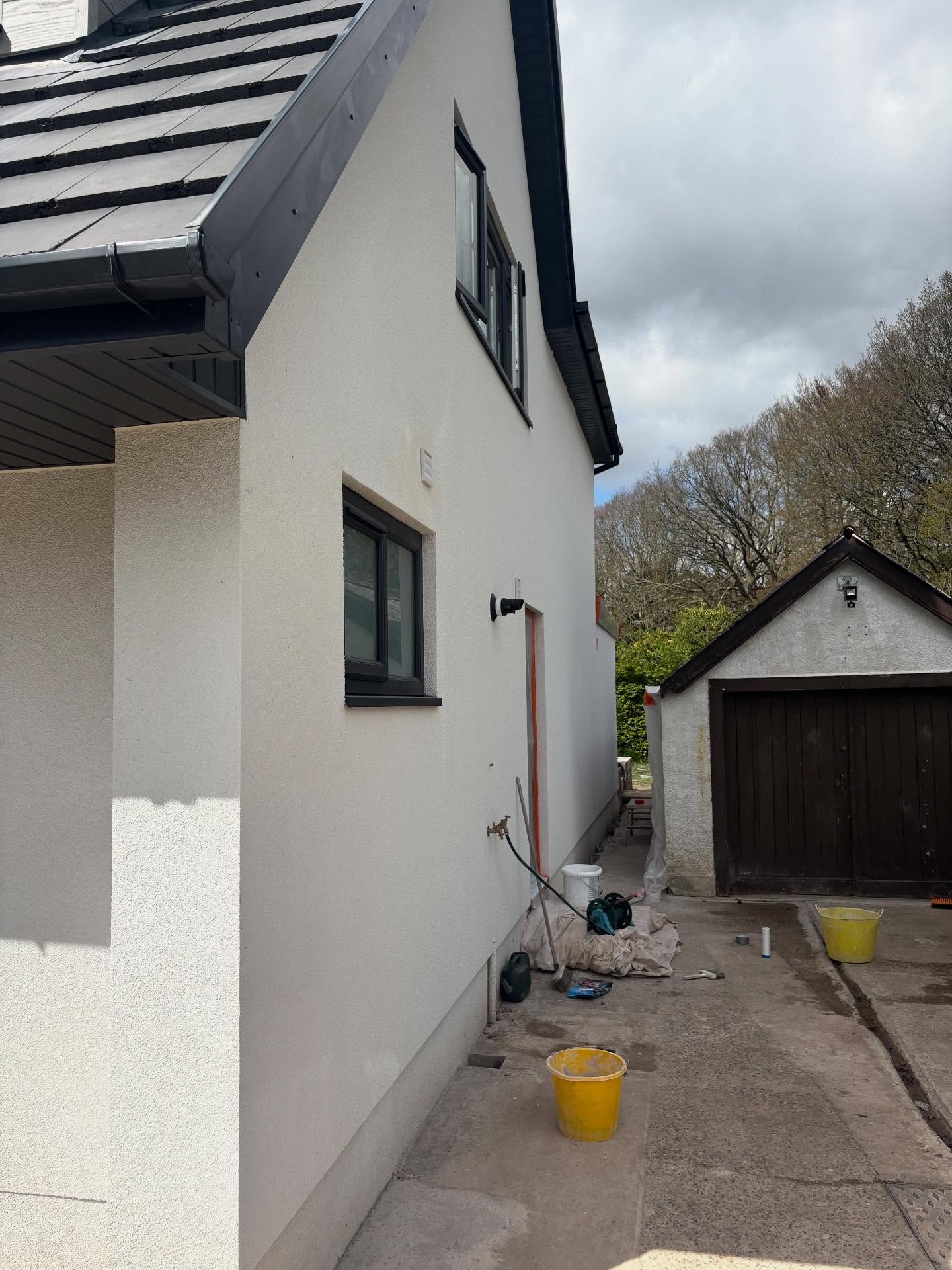 Side wall of the house in white render with the garage behind