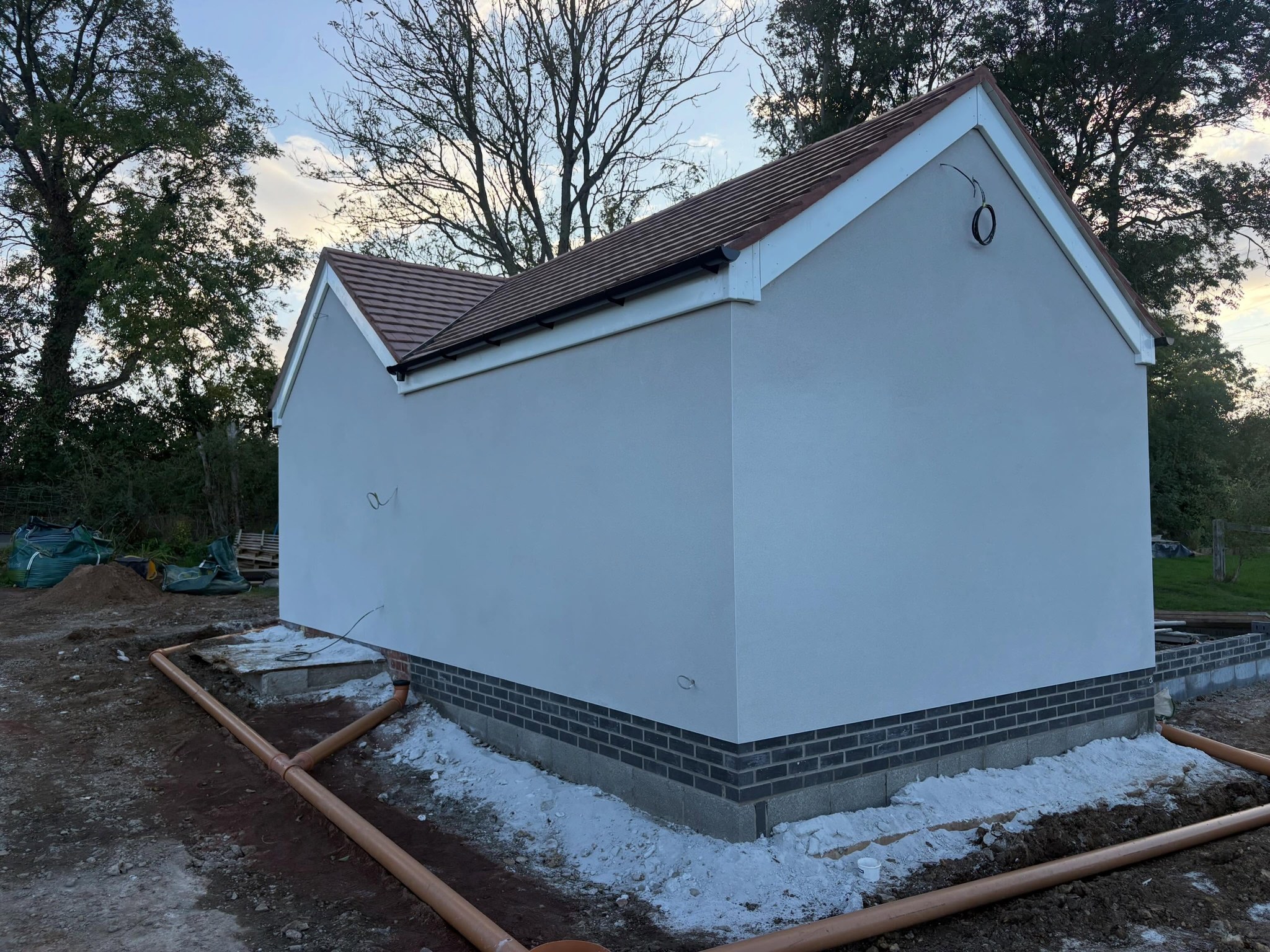 Rendered gable at dusk with brick plinth below